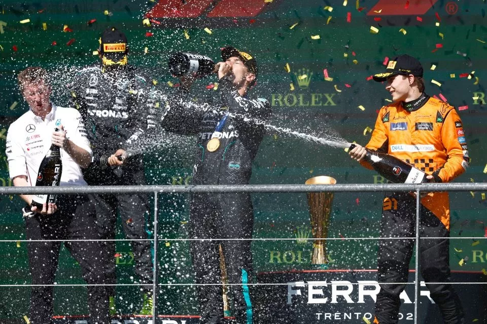 The Mercedes trophy delegate, Lewis Hamilton, Mercedes-AMG F1 Team, 2nd position, George Russell, Mercedes-AMG F1 Team, 1st position, Oscar Piastri, McLaren F1 Team, 3rd position, celebrate on the podium with Champagne