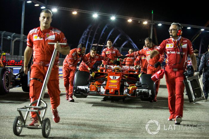El coche de Sebastian Vettel, Ferrari SF70H, es empujado por miembros del equipo.