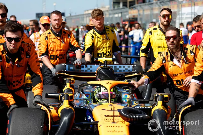 Mechanics push Lando Norris, McLaren MCL38, to his grid slot