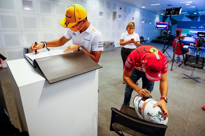 Lando Norris, McLaren, firma un libro para Jean Todt, President de la FIA, mientras Charles Leclerc, Ferrari, firma un casco