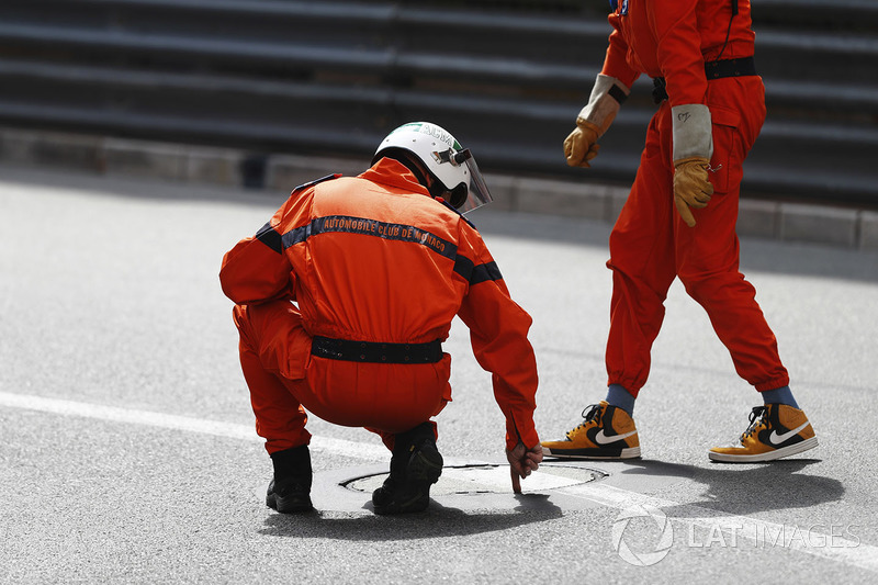 A marshal inspects a drain cover during a red flag period in FP2