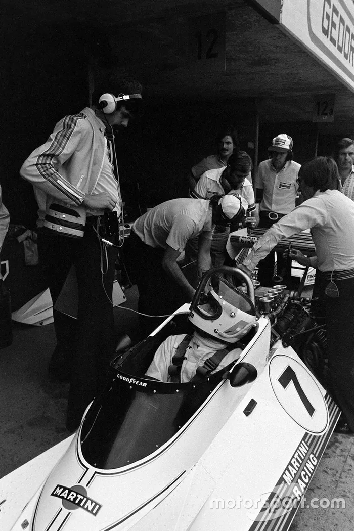 Los mecánicos trabajan en el Brabham BT44B Ford de Carlos Reutemann, mientras Gordon Murray habla con Reutemann y Bernie Ecclestone se apoya en el aro de rodamiento y observa